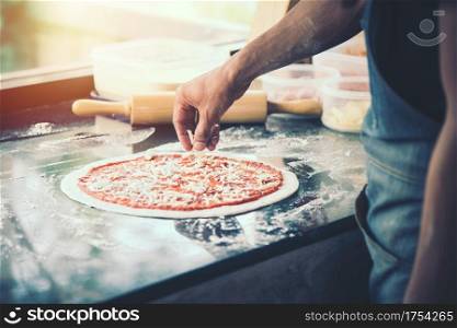 hand Chef preparing spread cheese on pizza on marble table, closeup making pizza