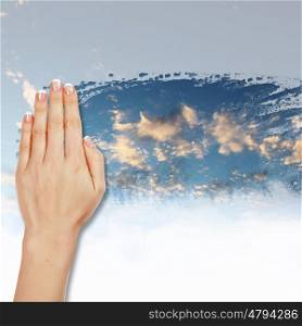 Hand cleaning window with blue sky and white clouds