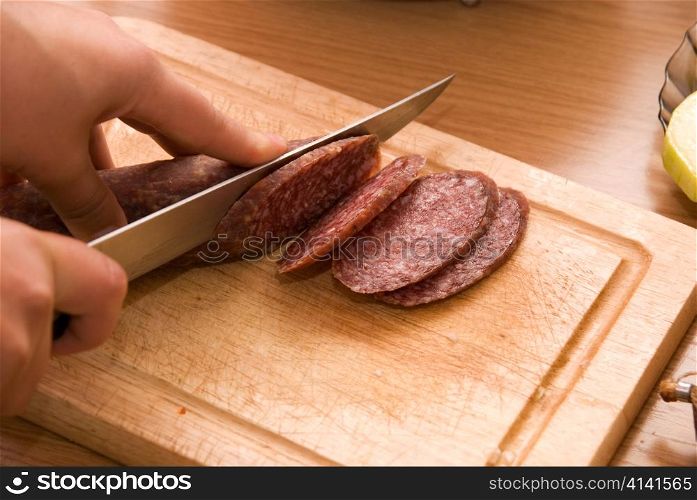 Hand closeup cuts salami with slice pieces at table