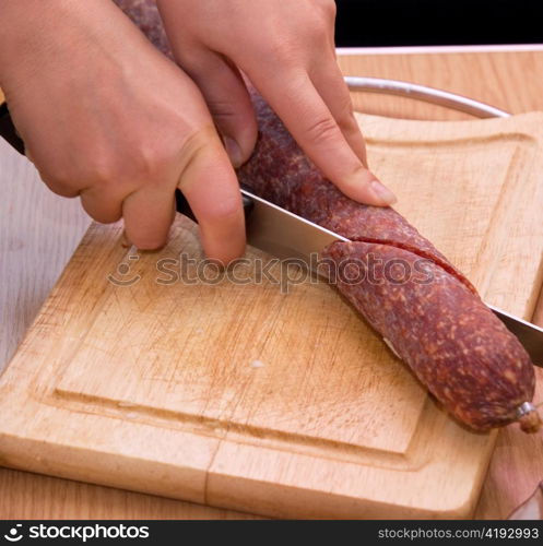 Hand closeup cuts salami with slice pieces at table