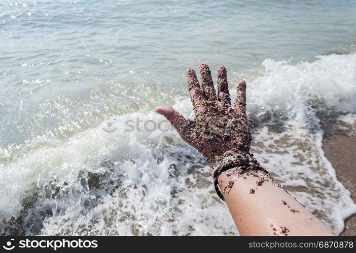Hand covered with beach sand. Sea and foam in the background.