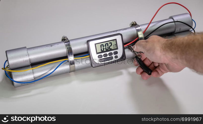 Hand cutting wire on pipe bomb with an lcd clock timer to trigger detonation on white background