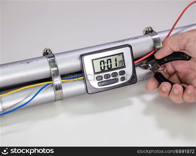 Hand cutting wire on pipe bomb with an lcd clock timer to trigger detonation on white background
