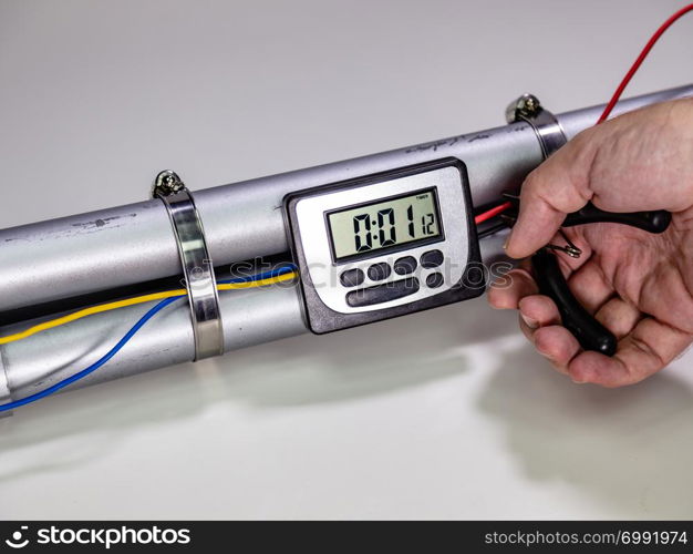 Hand cutting wire on pipe bomb with an lcd clock timer to trigger detonation on white background