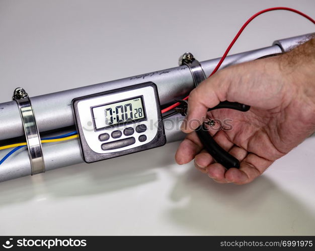 Hand cutting wire on pipe bomb with an lcd clock timer to trigger detonation on white background