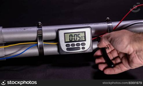 Hand cutting wire on pipe bomb with an lcd clock timer to trigger detonation on black background