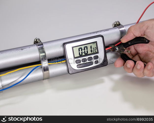 Hand cutting wire on pipe bomb with an lcd clock timer to trigger detonation on white background