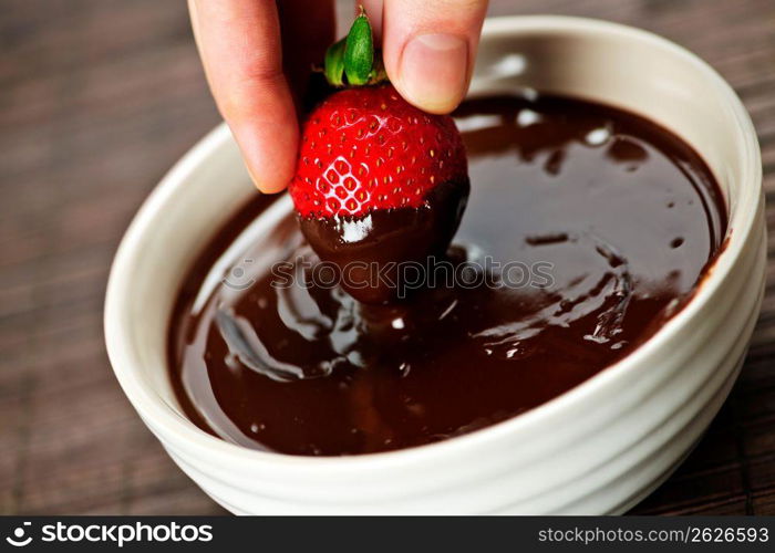 Hand dipping strawberry in chocolate