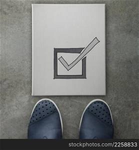 Hand drawn check mark icon on canvas board on front of business man feet as concept