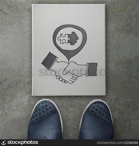 hand drawn handshake signon canvas board on front of business man feet as concept