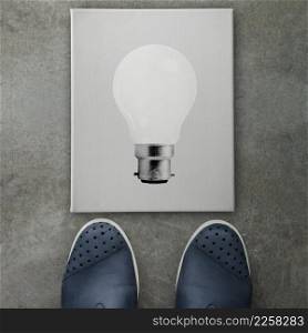 Hand drawn light bulb on dark canvas board front of business man feet as concept