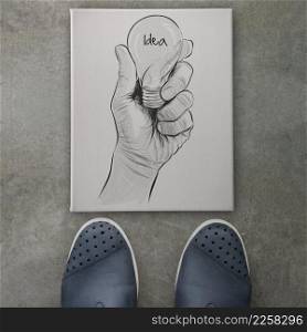 Hand drawn light bulb with IDEA word on canvas board front of business man feet as concept