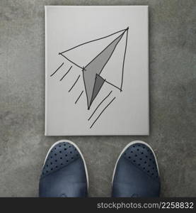 Hand drawn paper plane icon on canvas board on front of business man feet as concept