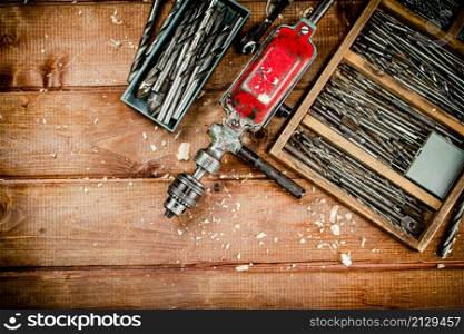 Hand drill with various drills. On a wooden background. High quality photo. Hand drill with various drills.