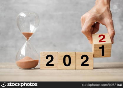 hand flipping block 2021 to 2022 text with hourglass on table. Resolution, time, plan, goal, motivation, reboot, countdown and New Year holiday concepts