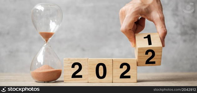 hand flipping block 2021 to 2022 text with hourglass on table. Resolution, time, plan, goal, motivation, reboot, countdown and New Year holiday concepts