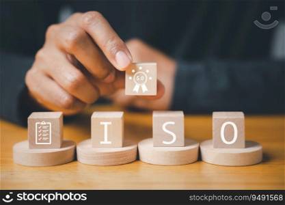 Hand flipping smart globe ISO icons with check mark guarantee icon on wooden cube, symbolizing quality control certification concept. Businessman in the background represents corporate management