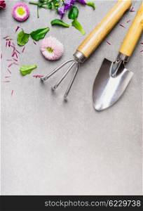 Hand garden rake and shovel with flowers plant on gray stone background, top view, place for text. Summer gardening concept