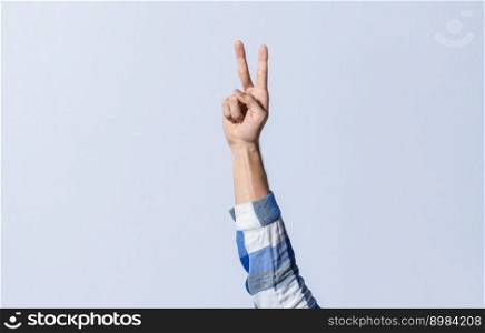 Hand gesturing the letter V in sign language on an isolated background. Man’s hand gesturing the letter V of the alphabet isolated. Letter V of the alphabet in sign language