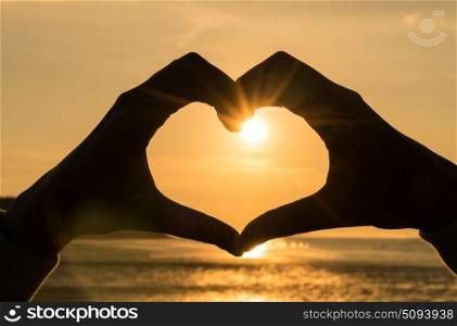 Hand heart frame shape silhouette made against the sun & sky of a sunrise or sunset on a deserted empty beach
