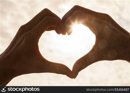 Hand heart shape silhouette made against the sun &amp; sky of a sunrise or sunset