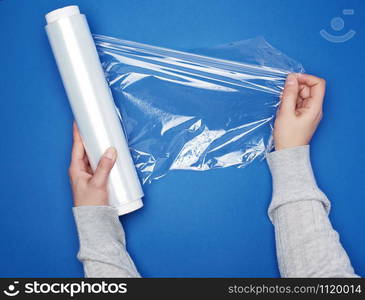 hand hold a large roll of wound white transparent film for wrapping food, top view, blue background