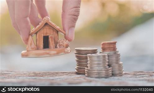Hand hold home model with coins stack on wood table sunlight background