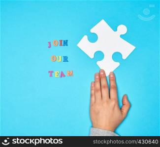 hand hold large white puzzles and the inscription join our team on a blue background, concept of recruitment