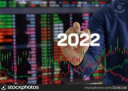 hand hold pen touching screen digital virtual futuristic interface 2022 New year candlestick graph chart auto trade, business finance investment stock exchange market concept background.