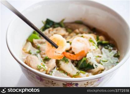 Hand hold shrimp with chopsticks of thai style spicy noodles soup