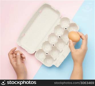 hand hold whole brown chicken egg and paper tray on a pink-blue background, top view