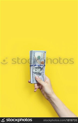 Hand holding a big stack of banknotes isolated on yellow background. Wealth or loan concept. Vertical banner.. Hand holding a big stack of banknotes isolated on yellowbackground. Wealth or loan concept. Vertical banner