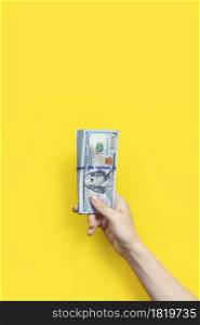 Hand holding a big stack of banknotes isolated on yellow background. Wealth or loan concept. Vertical banner.. Hand holding a big stack of banknotes isolated on yellowbackground. Wealth or loan concept. Vertical banner