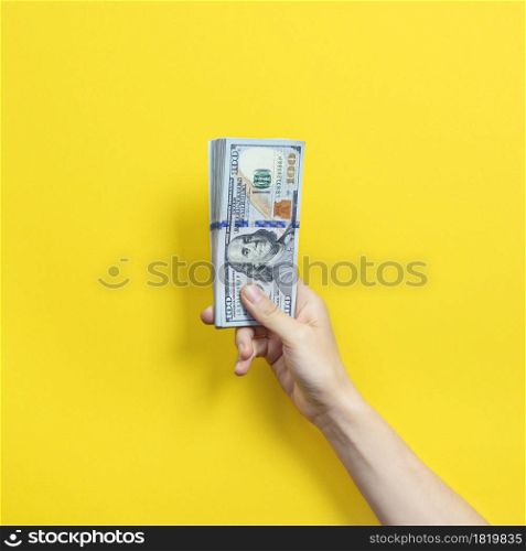 Hand holding a big stack of banknotes isolated on yellow background. Wealth or loan concept
