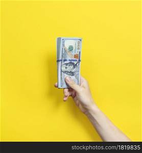 Hand holding a big stack of banknotes isolated on yellow background. Wealth or loan concept