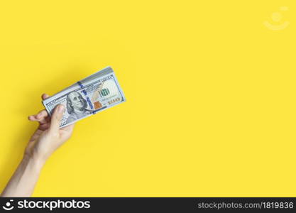 Hand holding a big stack of banknotes isolated on yellow background. Wealth or loan concept. Banner with copy space.. Hand holding a big stack of banknotes isolated on yellow background. Wealth or loan concept. Banner with copy space