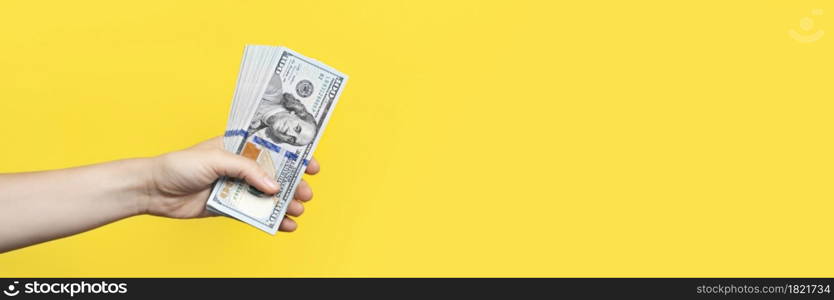 Hand holding a big stack of banknotes isolated on yellow background. Wealth or loan concept. Long Banner with copy space. Hand holding a big stack of banknotes isolated on yellow background. Wealth or loan concept. Long Banner with copy space.