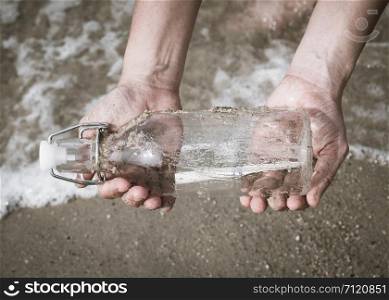 Hand holding a bottle with a letter inserted inside by the sea.