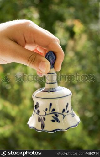 Hand holding a ceramic bell on a green background