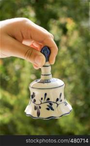 Hand holding a ceramic bell on a green background
