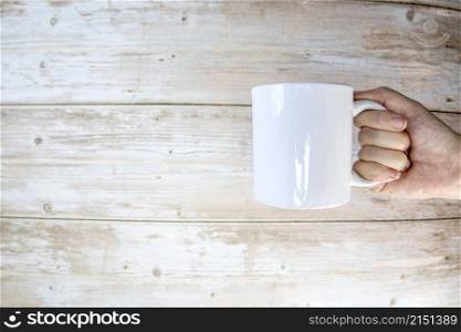 Hand holding a ceramic mug blank on wooden background with copy space, space for text. Hand holding a ceramic mug blank on wooden background with copy space,