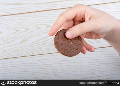 Hand holding a chocolate covered cookie on a wooden background