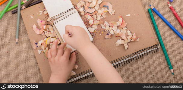 Hand holding a color pencil on spiral notebooks with pencil trash