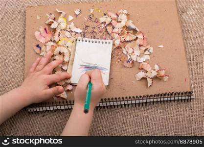Hand holding a color pencil on spiral notebooks with pencil trash