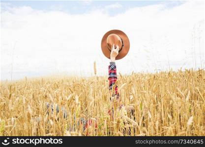Hand holding a cowboy hat over a field of wheat                               
