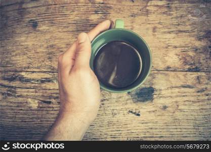 Hand holding a cup of black coffee at a table