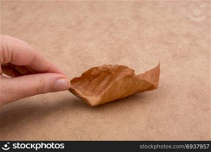 Hand holding a dry autumn leaf in hand on a brown background