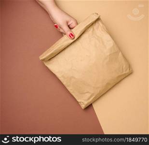 hand holding a full paper bag of brown kraft paper ona brown background, close up