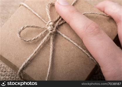 Hand holding a gift box of brown color on linen canvas