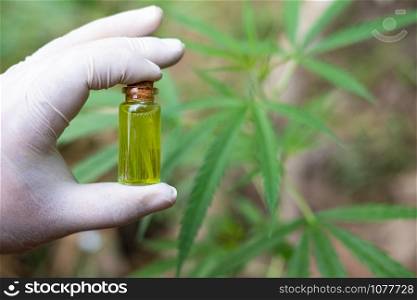 Hand holding a glass bottle with CBD oil and cannabis leaf at the background, medical marijuana concept